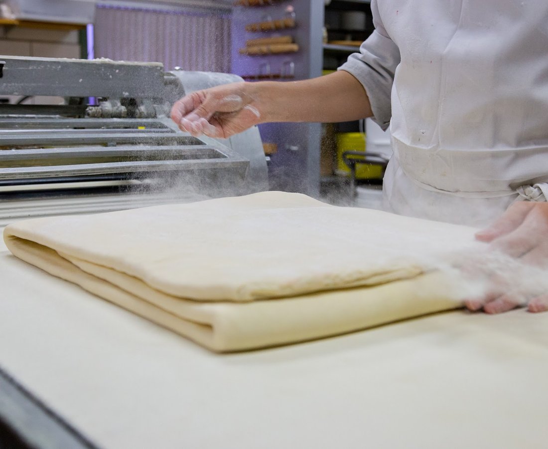 Des mains tournant une pâte feuilletée sur le plan de travail