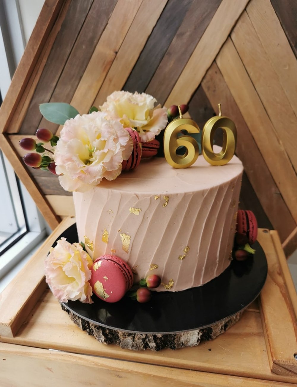 Un gâteau rose poudré avec un 60 doré, des fleurs fraîches et des macarons