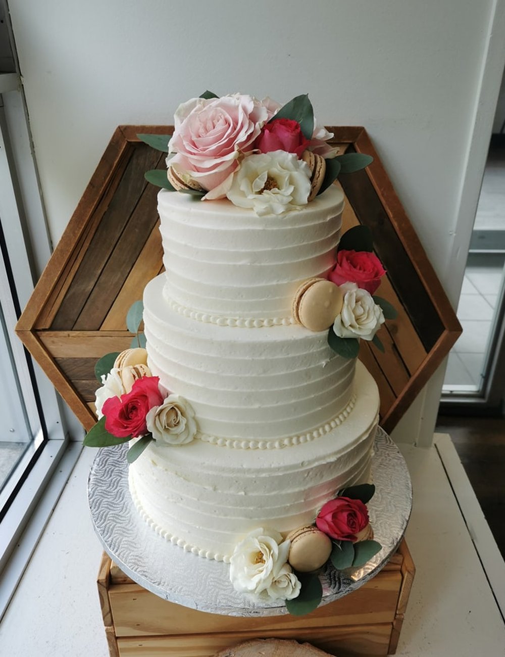 Un gâteau à trois étages, glaçage blanc et roses en sucre