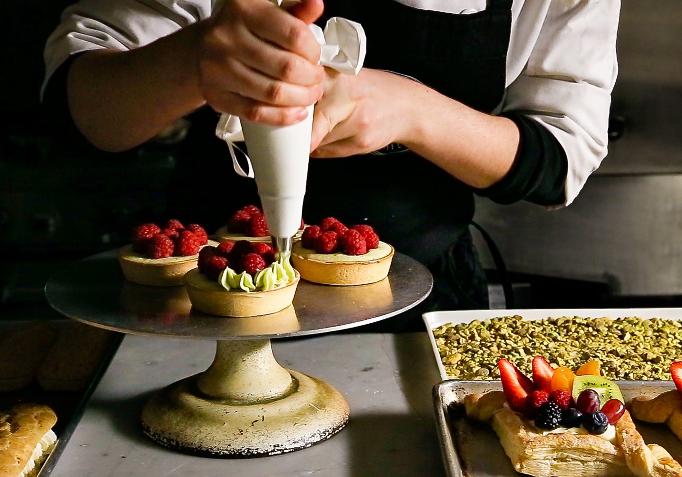Deux mains dressant la crème sur des tartelettes, au laboratoire de la pâtisserie